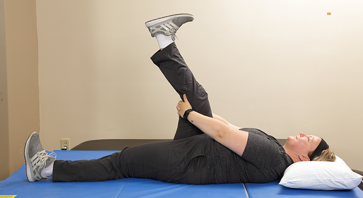 A patient demonstrates the first part of the hamstring stretch back pain exercise